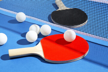 Ping pong rackets, balls and net on blue background, closeup
