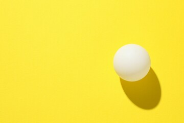 One ping pong ball on yellow background, top view. Space for text