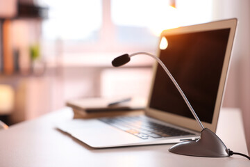Microphone and laptop on white desk in office. Space for text