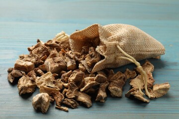 Pieces of dry chicory roots and sack on blue wooden table, closeup