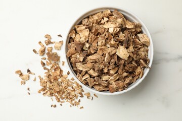 Pieces of dry chicory roots in bowl on white table, top view