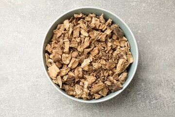 Pieces of dry chicory roots in bowl on gray textured table, top view