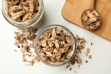 Pieces of dry chicory roots in bowl, jar and spoon on white table, flat lay