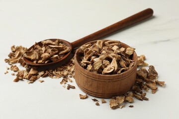 Pieces of dry chicory roots in bowl and spoon on white table