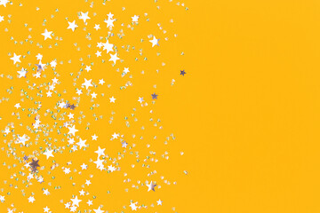Silver stars and crystals confetti on a yellow background. Glowing concept with copy space.
