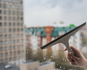 A woman washes a window with a scraper. 