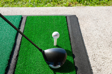 Golf club driver with ball on tee at driving range.