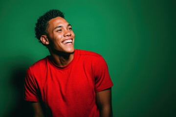 Fototapeta premium Smiling young adult wearing a bright red shirt, looking to the side, against a plain backdrop. The expression is cheerful and relaxed, with a lively and dynamic pose