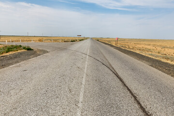 Straight asphalt road stretches through flat arid landscape in Atyrau Region Kazakhstan