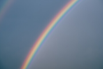 Fototapeta premium Colorful rainbow arching across a cloudy sky, a beautiful meteorological phenomenon appearing after rainfall, creating a vibrant spectrum of colors against the muted backdrop