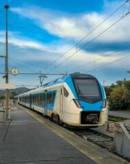 Fototapeta premium Platform with standing train in blue with white color, on the background of blue sky with white clouds