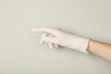 Doctor in medical glove pointing at something on light grey background, closeup