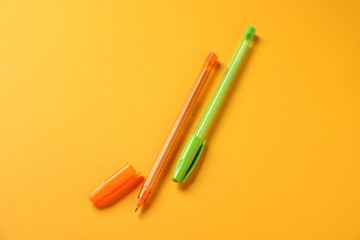 Stylish pens on orange background, above view