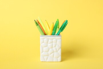 Ballpoint pens in holder on yellow background, closeup