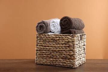 Obraz premium Clean towels in basket on wooden table against brown background