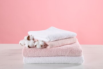 Stack of clean towels and cotton flowers on light marble table against pink background