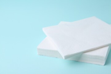Stack of disposable paper handkerchiefs on light blue background, closeup. Space for text