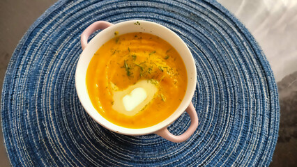 Orange pumpkin soup, in a round bowl with handles on a blue round napkin. Delicious homemade pumpkin soup with butter