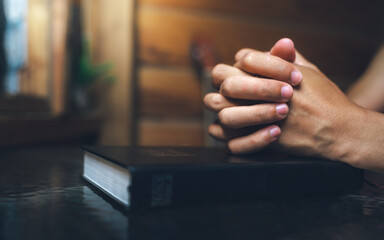 Close up of a man praying, hands clasped together on Bible, devotional concept.