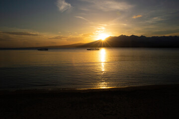 beautiful dramatic landscape of sunset on sea beach with silhouette of boat