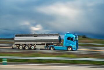 Tanker truck driving on a highway, panning shot with motion blur, side view.