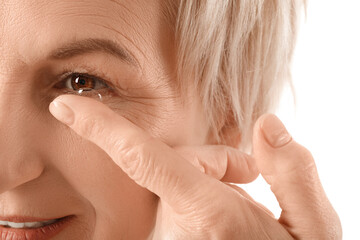 Mature woman putting in contact lenses on white background, closeup