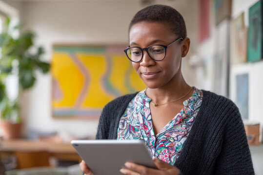 Woman browsing NFT marketplace on tablet, bright art-inspired interior, calm and professional setting.