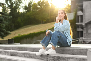 Beautiful young woman with stylish sunglasses sitting on stairs outdoors