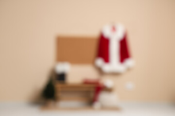 Santa Claus suit on hanger, bench with boots and frame on beige wall in room. Blurred view