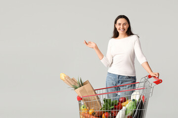 Beautiful young happy woman with full shopping cart on grey background