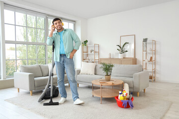 Young man vacuuming carpet and listening to music in room