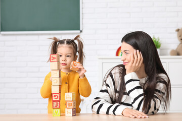 Cute little girl with teacher and wooden cubes learning alphabet at home