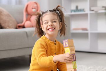 Cute little girl with wooden cubes learning alphabet at home