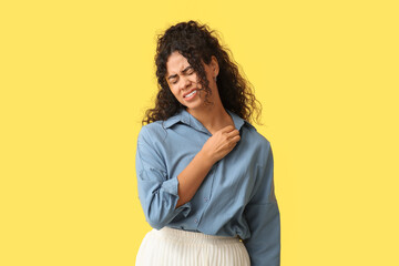 Young African-American woman suffering from skin allergy on yellow background