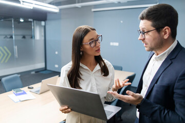 Businessman executive manager ceo talking to female coworker and using laptop, professional partners discussing business plan at board meeting room, free space