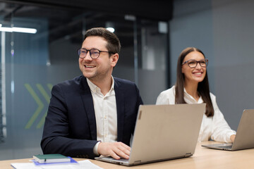 Happy businessman listening to discussion in an office boardroom, working on laptop, business...