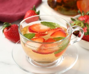 Aromatic fruit tea with strawberries and mint on white marble table, closeup