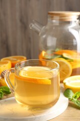 Aromatic fruit tea in glass cup, teapot, orange, lemon, honey and mint on wooden table, closeup