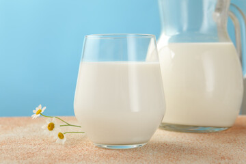 Fresh milk and flowers on table against light blue background, closeup