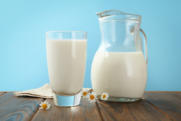 Fresh milk and flowers on wooden table against light blue background, closeup