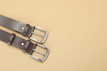 Two leather belts on beige background, flat lay. Space for text