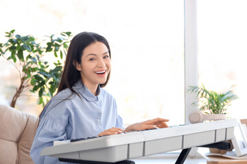 Young woman playing synthesizer in armchair at home