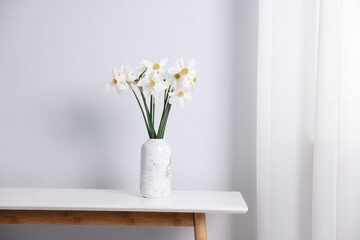 Beautiful daffodils in vase on white table indoors