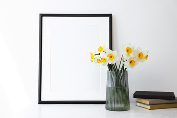 Beautiful daffodils in vase, picture frame and books on white table indoors