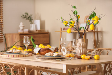 Stylish table setting decorated with many fresh citruses and beautiful lemon tree branches near beige wall in dining room