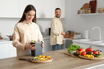 Young woman with compost bin and vegetable scraps during cooking in kitchen