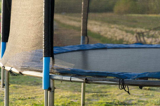 Trampoline with safety net and blue padding in backyard, providing recreational fun and bounce for children and family activities