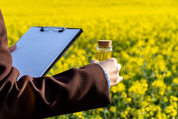 Agronomist Inspecting Canola Oil Quality in Field Holding Clipboard and Vial with Cork Stopper