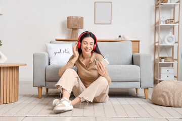 Beautiful young woman with modern power bank and headphones listening to music at home