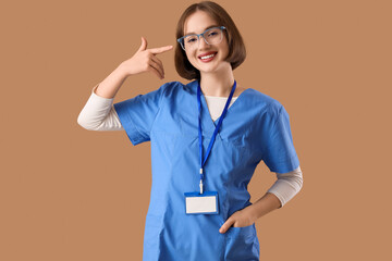 Young happy female ophthalmologist pointing at new eyeglasses on brown background